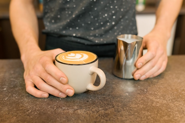 Nahaufnahme der Lattekunst, Hände von barista und Eisenbecher mit Milch