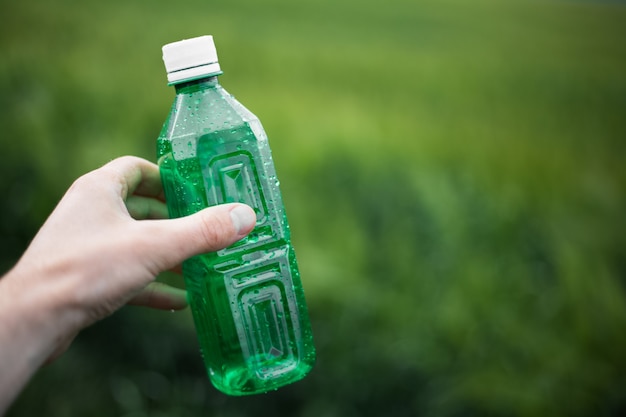 Nahaufnahme der männlichen Hand, die Einwegplastikflasche der grünen Farbe hält