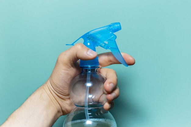 Nahaufnahme der männlichen Hand, die Sprühflasche zur Reinigung mit blauer Pumpe hält