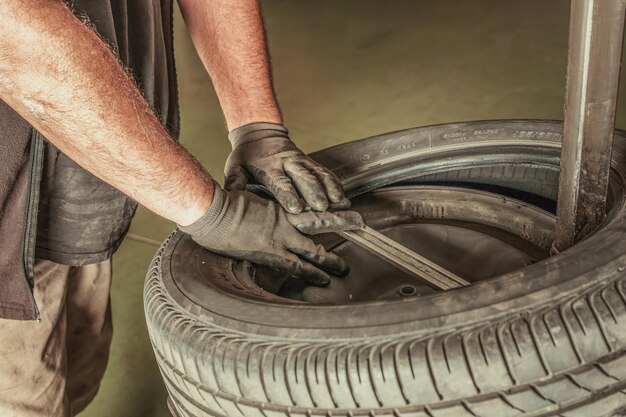 Nahaufnahme der mit Handschuhen geschützten Hände eines Mannes, der einen Reifen in einer schmutzigen Garage repariert