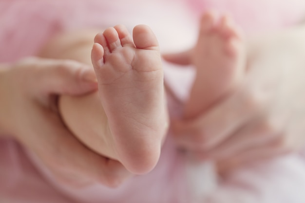 Nahaufnahme der Mutter Hände halten niedlichen kleinen Baby Füße, zeigt Baby Fuß. Rosa Hintergrund. Horizontal.