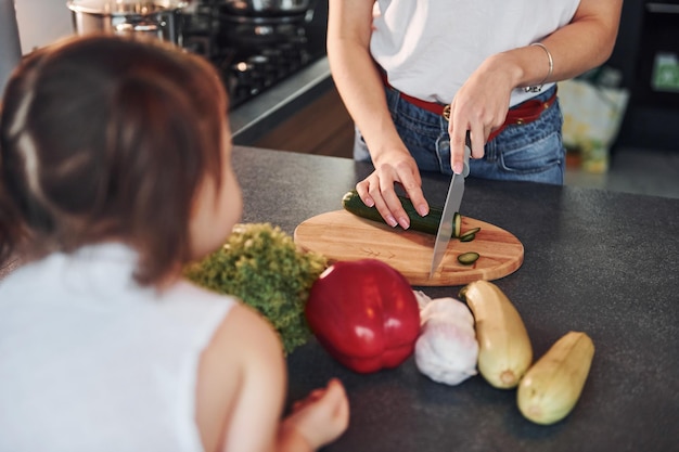 Nahaufnahme der Mutter mit ihrer kleinen Tochter, die drinnen in der Küche Essen zubereitet