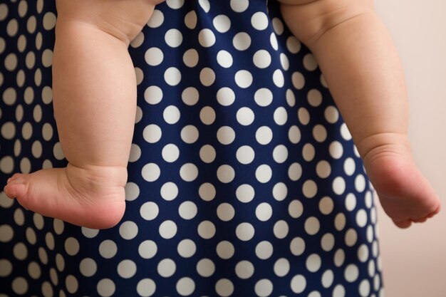 Nahaufnahme der nackten Füße des Babys auf dem Hintergrund des Kleides meiner Mutter mit Tupfen