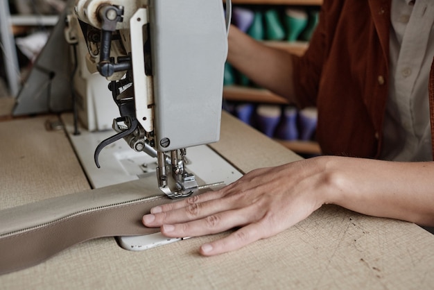 Nahaufnahme der Näherin, die am Tisch sitzt und Kleidung an der Nähmaschine näht