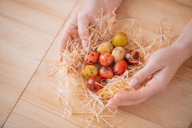 Nahaufnahme der nicht wiedererkennbaren Frau, die orange und gelbe Osterwachteleier in Heu am Tisch einwickelt