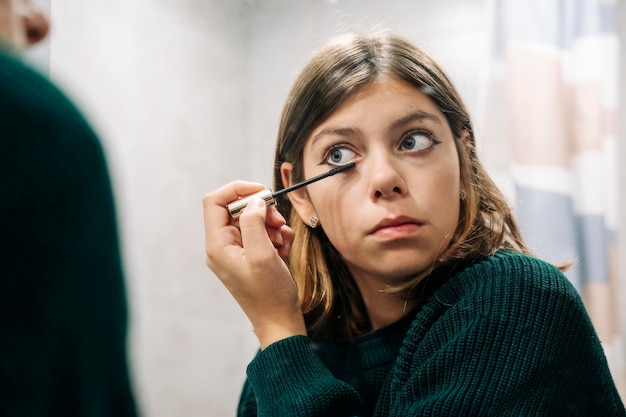 Nahaufnahme der Reflexion eines Teenagers, der Wimperntusche auf die Wimpern aufträgt