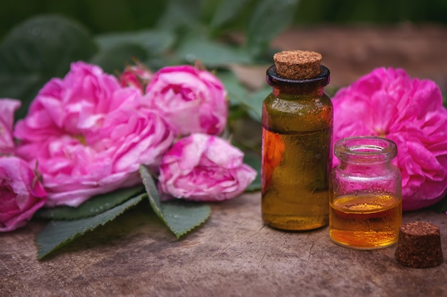 Nahaufnahme der Rose ätherisches Öl Flasche mit fallenden Blättern auf Holzuntergrund. Selektiver Fokus