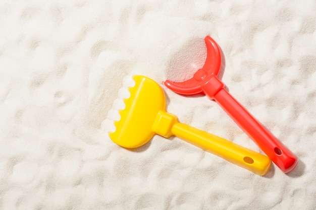 Nahaufnahme der roten Schaufel und des gelben Rechen auf Sand.