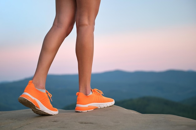 Nahaufnahme der schlanken Beine der jungen Frau in leuchtend orangefarbenen Turnschuhen, die im Sommer auf dem Bergwanderweg gehen. Aktive Lebensweise und Bewegung im Frischluftkonzept.