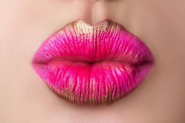 Nahaufnahme der schönen Frauenlippen, die einen Kuss blasen. Modernes Make-up in Pink und Gold. Studioaufnahme. Lippen Kosmetik, modernes Make-up oder Liebeskonzept