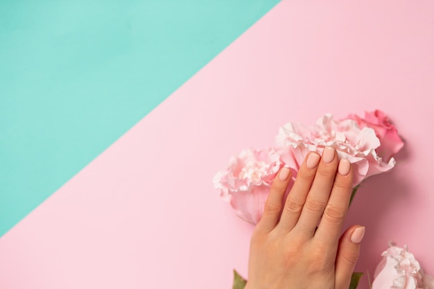 Foto nahaufnahme der schönen weiblichen hand mit einer zarten maniküre auf den nägeln auf der rosa blume. auf einem zweifarbigen pastellblauen und rosa hintergrund kopieren sie platz. pflege, beauty, spa, salonkonzept