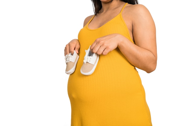 Nahaufnahme der schwangeren Frau, die Babyschuhe auf Bauch hält. Konzept für Schwangerschaft, Mutterschaft und Erwartung.