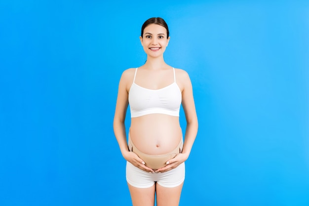Nahaufnahme der schwangeren Frau in Unterwäsche, die elastischen Schwangerschaftsverband trägt, um den Schmerz an der gelben Oberfläche mit Kopierraum verschwinden zu lassen