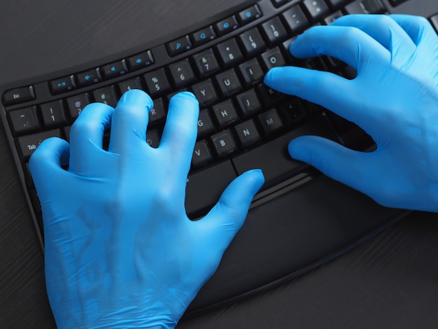 Nahaufnahme der schwarzen Computertastatur und der Hände in den blauen Latexhandschuhen.