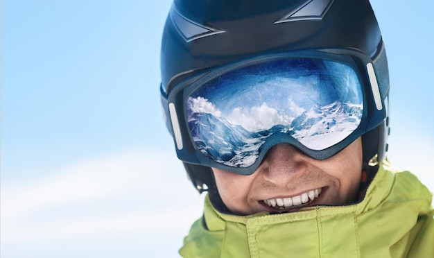 Nahaufnahme der Skibrille eines Mannes mit der Reflexion der verschneiten Berge.