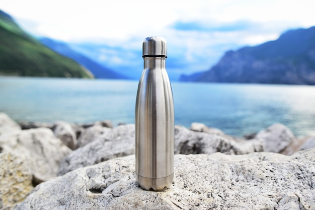 Nahaufnahme der stählernen Öko-Thermowasserflasche auf dem Hintergrund des Sees in den Bergen