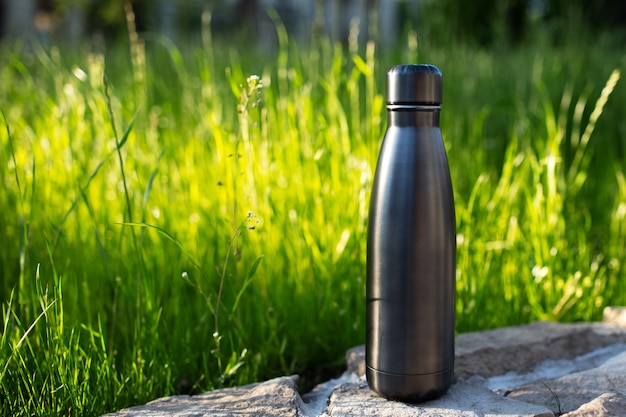 Nahaufnahme der Stahlthermowasserflasche schwarz auf dem Hintergrund des grünen Grases mit Kopienraum. Mehrwegflaschen Zero Waste Eco Concept plastikfrei.