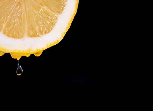 Nahaufnahme der Vorderansicht einer halben Zitrone auf schwarzem Hintergrund mit mehreren Tropfen Saft fallen