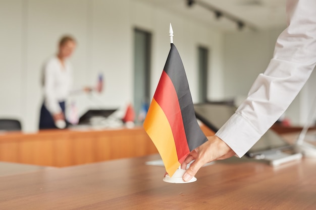 Nahaufnahme der weiblichen Assistentin, die deutsche Flagge auf Tisch setzt, während Konferenzraum für internationales Geschäftsereignis vorbereitet,