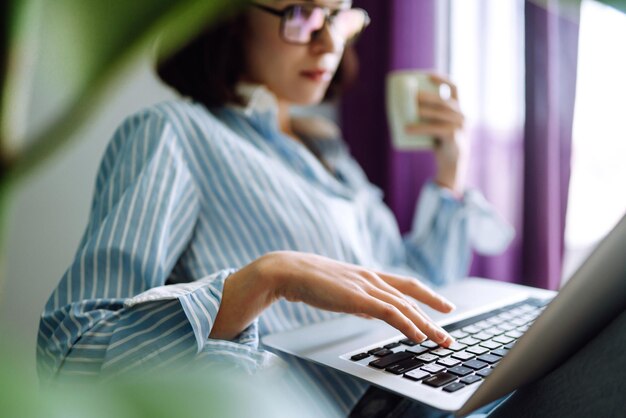 Nahaufnahme der weiblichen Hände auf der Tastatur. Junge Freiberuflerin, die zu Hause mit Laptop arbeitet.