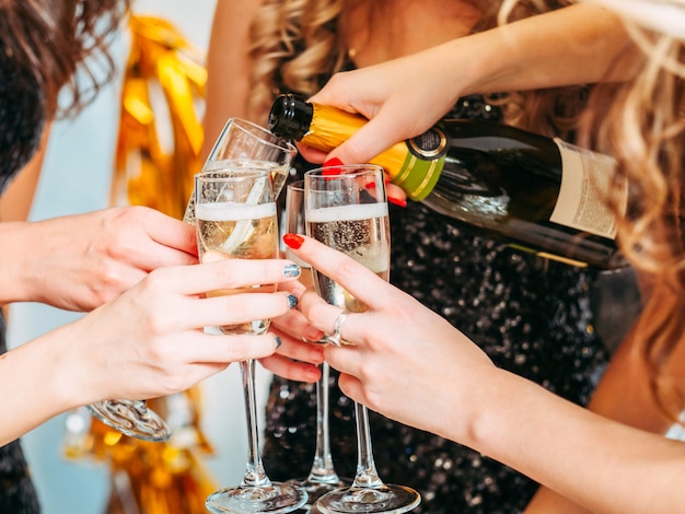 Nahaufnahme der weiblichen Hände, die Gläser halten, Mädchen, das Champagner gießt, um zu ihrem Geburtstag mit Freunden zu trinken.