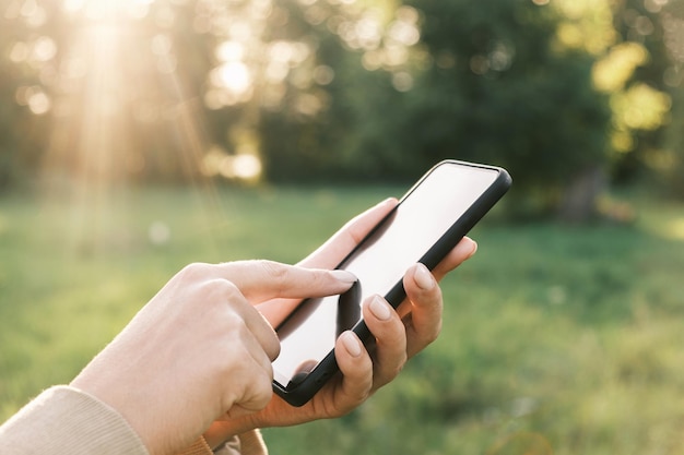 Nahaufnahme der weiblichen Hände mit einem Smartphone Natur Hintergrund Frau mit Handy im Sonnenuntergang im Freien Nicht erkennbare Person berühren Smartphone-Bildschirm Unbekanntes Mädchen mit Handy draußen