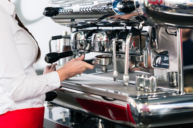 Nahaufnahme der weiblichen Hand auf dem Siebträger eines automatischen Kaffees