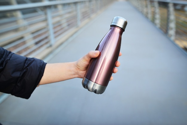 Nahaufnahme der weiblichen Hand, die wiederverwendbare, thermisch glänzende Stahlflasche für Wasser hält.