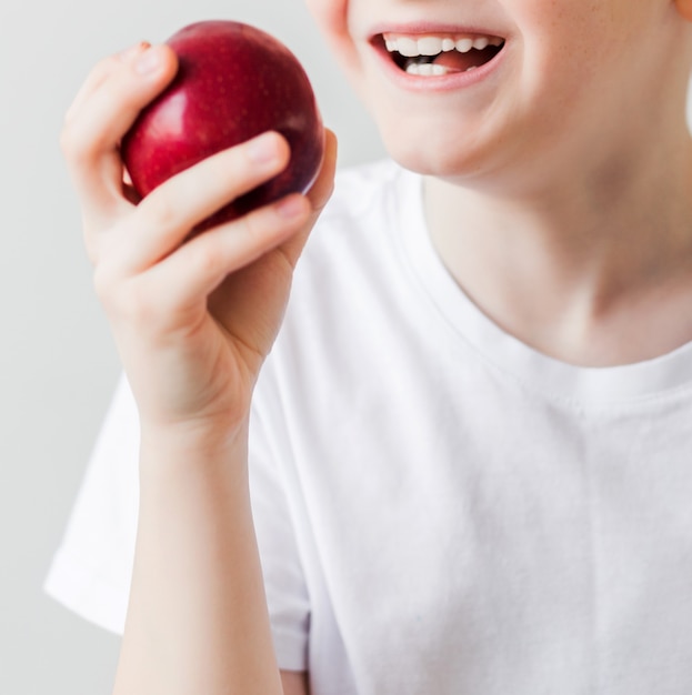 Nahaufnahme der Zähne eines gesunden Kindes und eines reifen roten Apfels. Vertikales Foto
