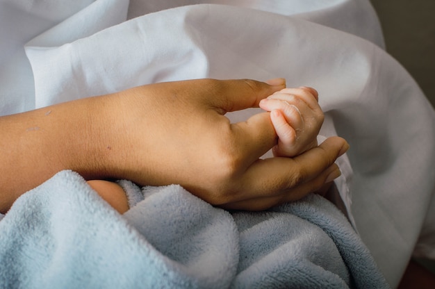 Nahaufnahme der zarten Hände des Neugeborenen in der Handfläche seiner Mutter