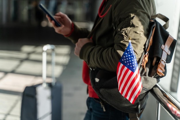 Nahaufnahme des amerikanischen Reisenden, der auf den Smartphone-Bildschirm schaut, während er auf seinen Flug wartet. Einwanderungskonzept