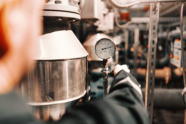 Nahaufnahme des Arbeiters in der Schwerindustrieanlage, der Luftdruck auf Kessel einstellt.