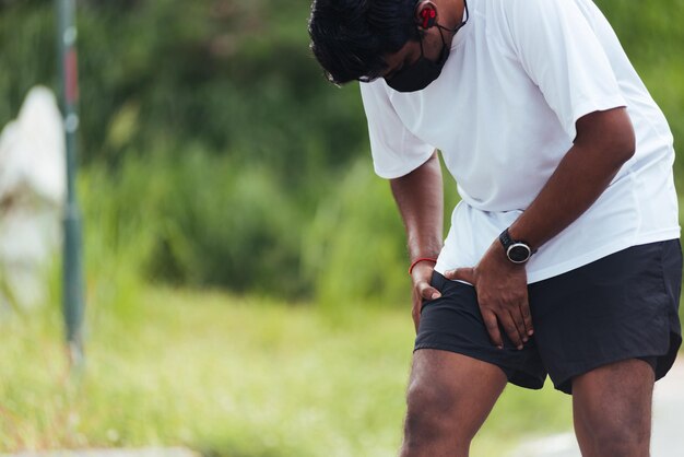 Nahaufnahme des asiatischen jungen Sportläufers, schwarzer Mann, Uhr, Hände, Gelenk, Bein, sie hat Oberschenkelschmerzen, während sie im Outdoor-Straßen-Gesundheitspark läuft, gesunder Trainingsverletzungsmuskel aus dem Trainingskonzept