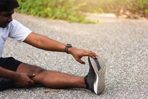 Nahaufnahme des asiatischen jungen Sportlers, Sportläufer, schwarzer Mann, der zuschaut, wie er sitzt, Zehenfüße zieht, Beine und Knie streckt, bevor er im Outdoor-Straßengesundheitspark läuft, gesunde Übung vor dem Trainingskonzept