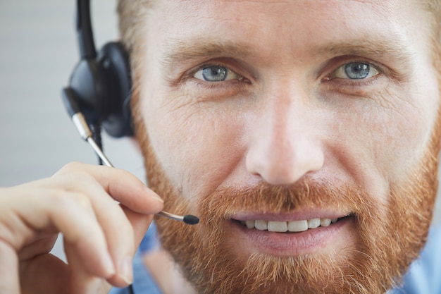 Nahaufnahme des bärtigen männlichen Betreibers in den Kopfhörern, die am Telefon lächeln und sprechen