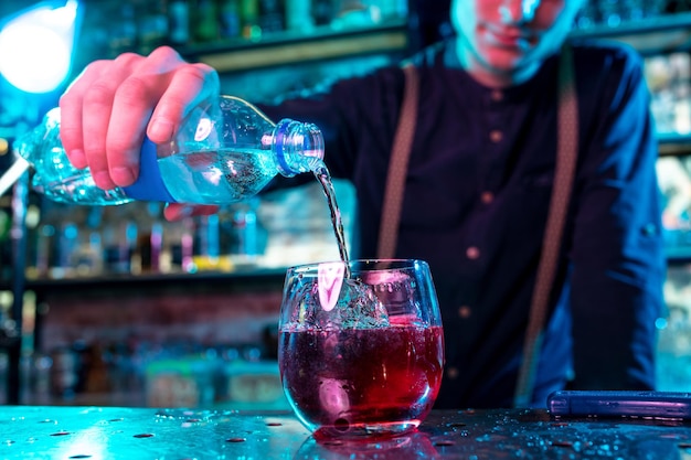 Nahaufnahme des Barmanns, der einen alkoholischen kalten Cocktail in buntem Neonlicht zubereitet