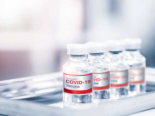 Nahaufnahme des Covid19-Impfstoffs mit rotem Etikett auf vier Flaschenfläschchen bei medizinischem Versuch auf dem Tisch im Labor