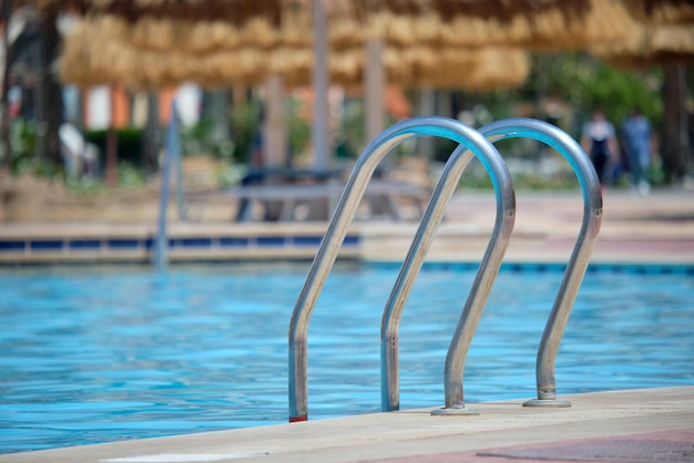 Nahaufnahme des Edelstahlhandlaufs des Swimmingpools, der in das klare Poolwasser der Schildkröte absteigt. Zugänglichkeit von Freizeitaktivitäten Konzept.