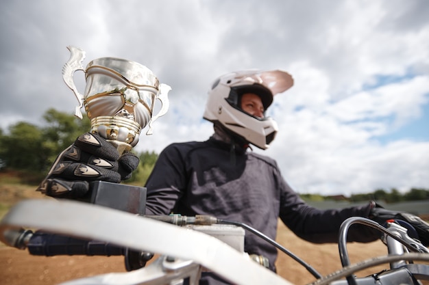 Nahaufnahme des erfolgreichen Motorradfahrers im Helm, der Motorrad-Meisterschaft reitet, die Motorrad fährt und Tasse hält