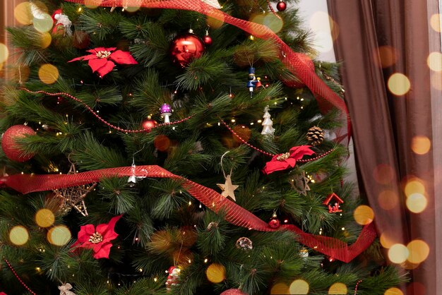 Nahaufnahme des festlich geschmückten Weihnachtsbaums mit Bällen und Spielzeug und Weihnachtssternblumen mit Bokeh