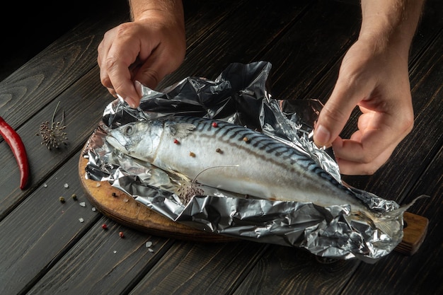 Nahaufnahme des Fischkochs, der Makrelen in der Küche zubereitet. Fisch vor dem Backen im Ofen in Folie einwickeln