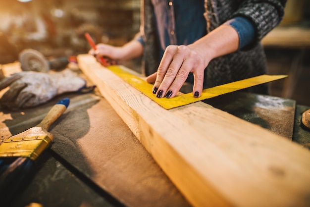 Nahaufnahme des fleißigen professionellen Zimmermanns, der mit einem Lineal arbeitet und Markierungen auf dem Holz macht