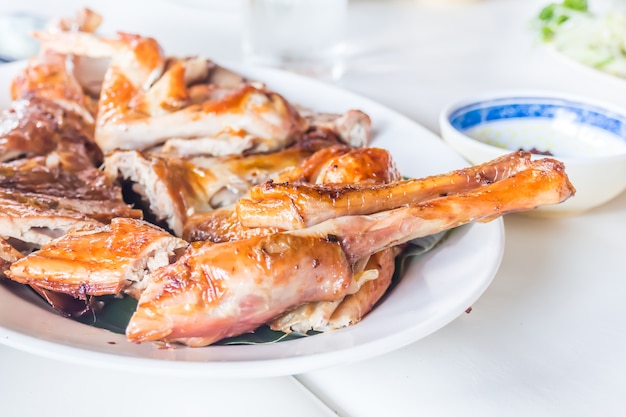 Nahaufnahme des gegrillten Huhns auf weißem Teller und Tabelle für Mittag- oder Abendessen.