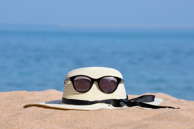Nahaufnahme des gelben Strohhuts und der schwarzen schützenden Sonnenbrille am Sandstrand an der tropischen Küste an einem warmen sonnigen Tag. Sommerferienkonzept.