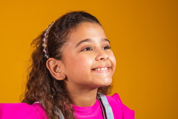 Nahaufnahme des gemischten Mädchens, das auf gelbem Hintergrund lächelt. Mischlingsmädchen mit glücklichem gewelltem Haar. Kindertag