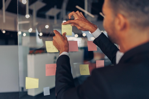 Nahaufnahme des Geschäftsmannes klebt Haftnotizen auf der Motivationstafel im modernen Büro