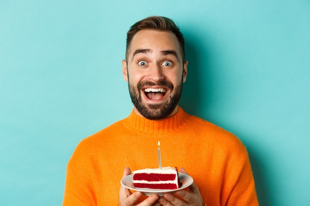 Nahaufnahme des glücklichen erwachsenen Mannes, der Geburtstag feiert, bday Kuchen mit Kerze hält und Wunsch macht, stehend