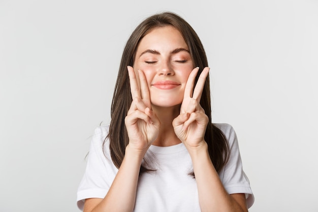 Nahaufnahme des glücklichen lächelnden brünetten Mädchens schließen Augen und zeigen Friedensgesten, Spaß haben.