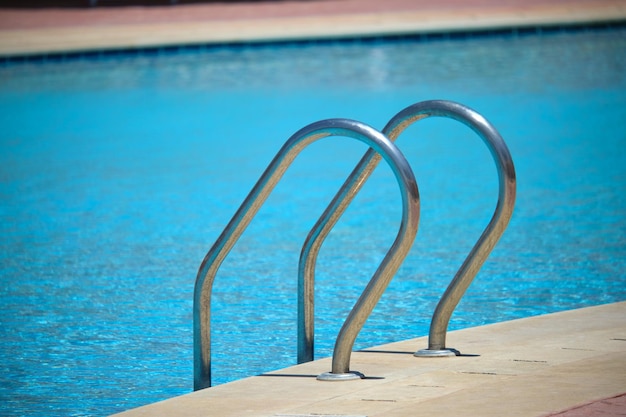 Nahaufnahme des Handlaufs aus Edelstahl des Swimmingpools, der in schildkrötenklares Poolwasser hinabsteigt Zugänglichkeit des Konzepts für Freizeitaktivitäten