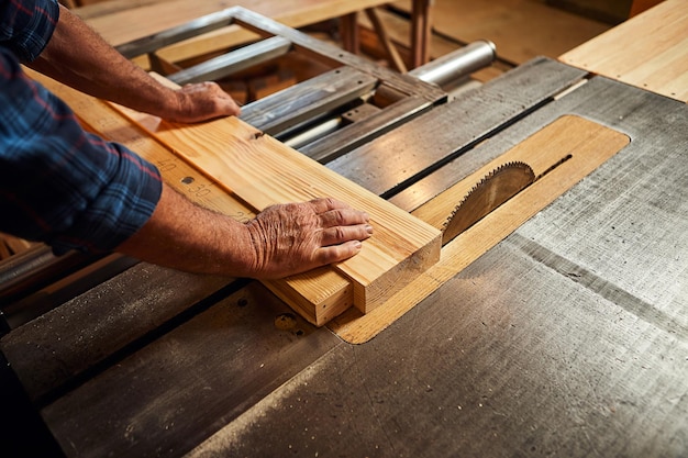 Nahaufnahme des Holzschneidetisches mit elektrischer Kreissäge Senior Professional Tischler in einheitlichem Schneiden von Holzbrettern in der Sägewerk-Zimmerei-Herstellung Sägemaschine